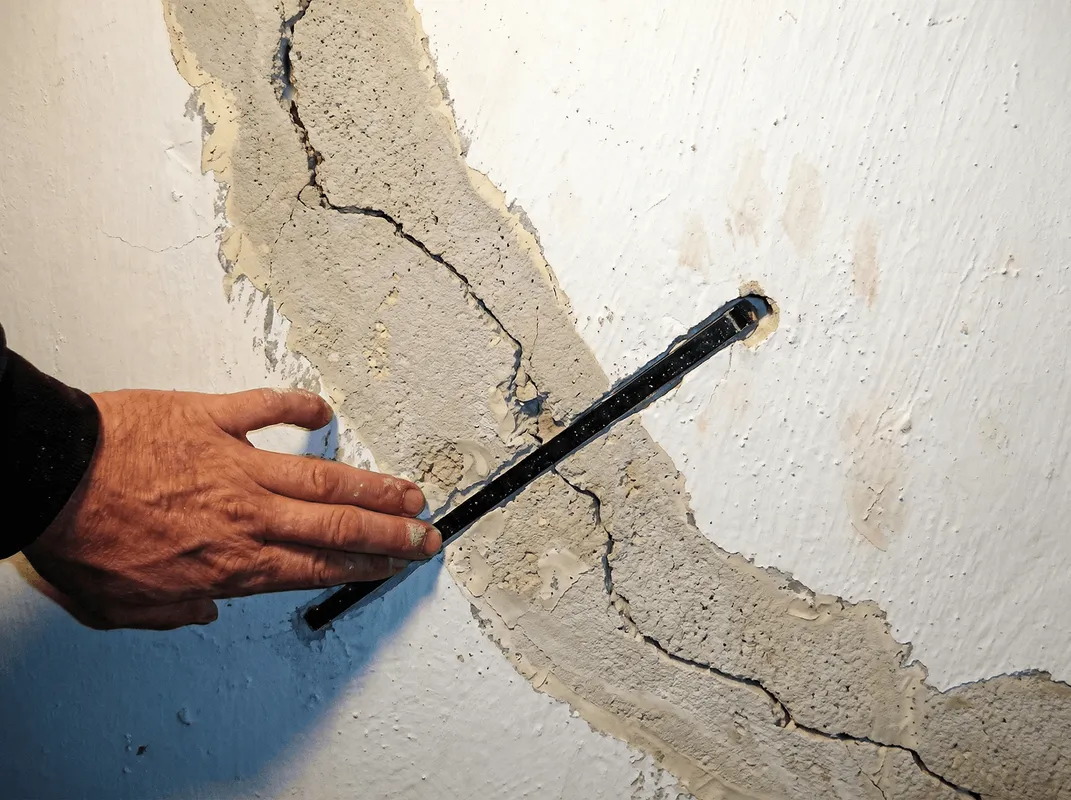 A wall with a large crack is being inspected by a professional in Indianapolis, IN